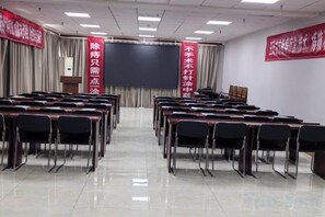 Una sala conferenze con file di tavoli e sedie, un podio e un grande schermo in prima fila.