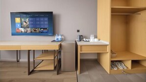 A modern, minimalist room with a wooden desk, a small refrigerator, a flat-screen TV mounted on the wall, and a built-in shoe storage unit. - GreenTree Zhixuan Hotel (Dezhou Bus Train Station Black Horse Antiques Debai Plaza) (Dezhou)