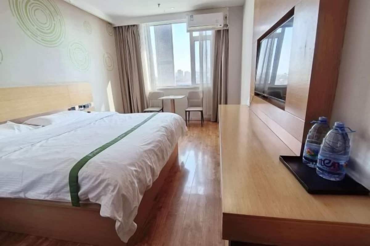 Hotellihuone, jossa on sänky, pieni pöytä, tuoleja, ikkuna ja juomavesiautomaatti.