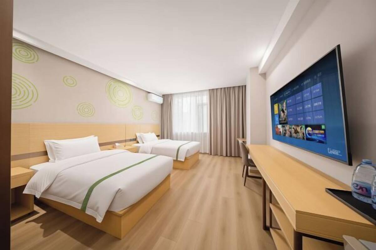 Hotellihuone, jossa on kaksi sänkyä, työpöytä, televisio ja ikkuna, jossa on verhot.