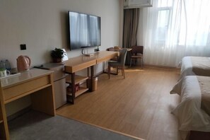 A hotel room with a wooden desk, a flat-screen TV, a bed, and a chair.
