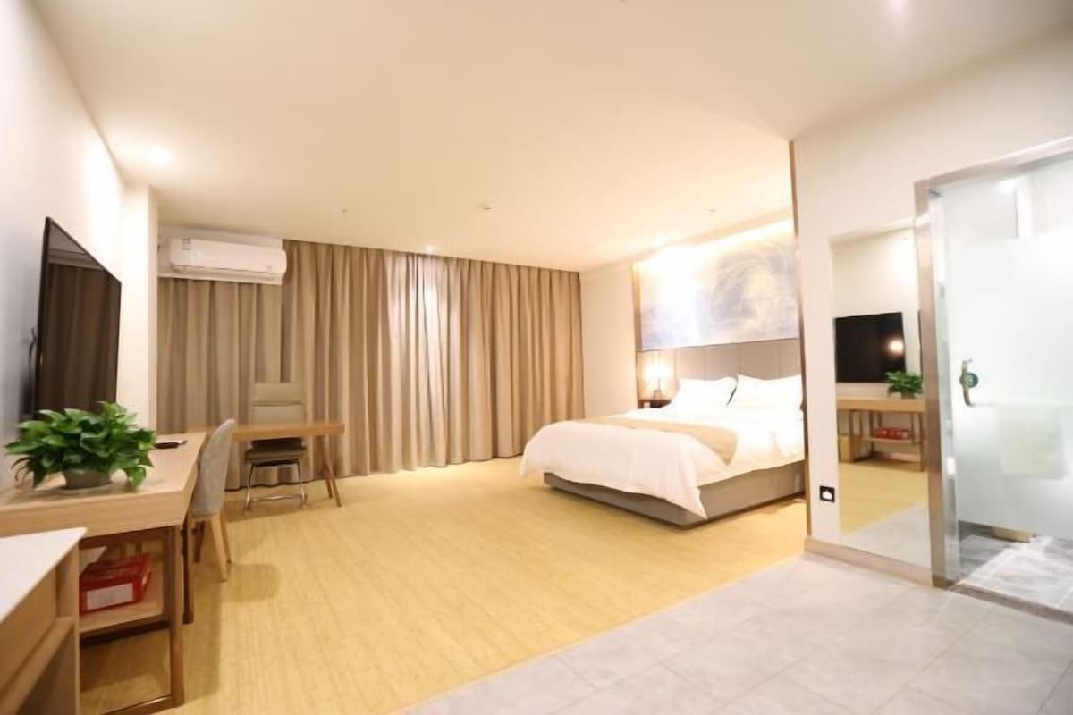 A hotel room with a bed, a desk, a chair, an air conditioning unit, and a curtain.