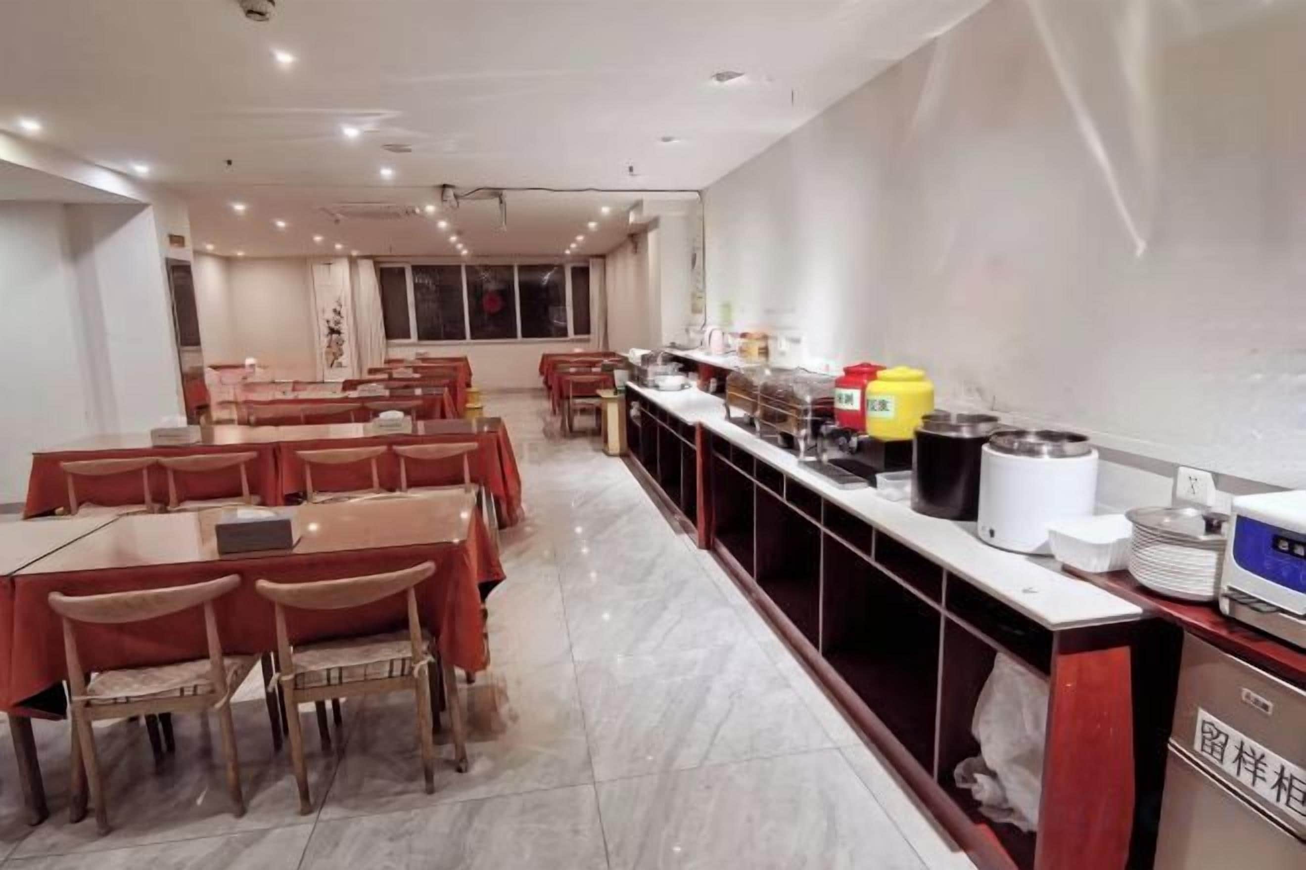 A dining area with tables and chairs, a buffet counter with food items, and a kitchen area.