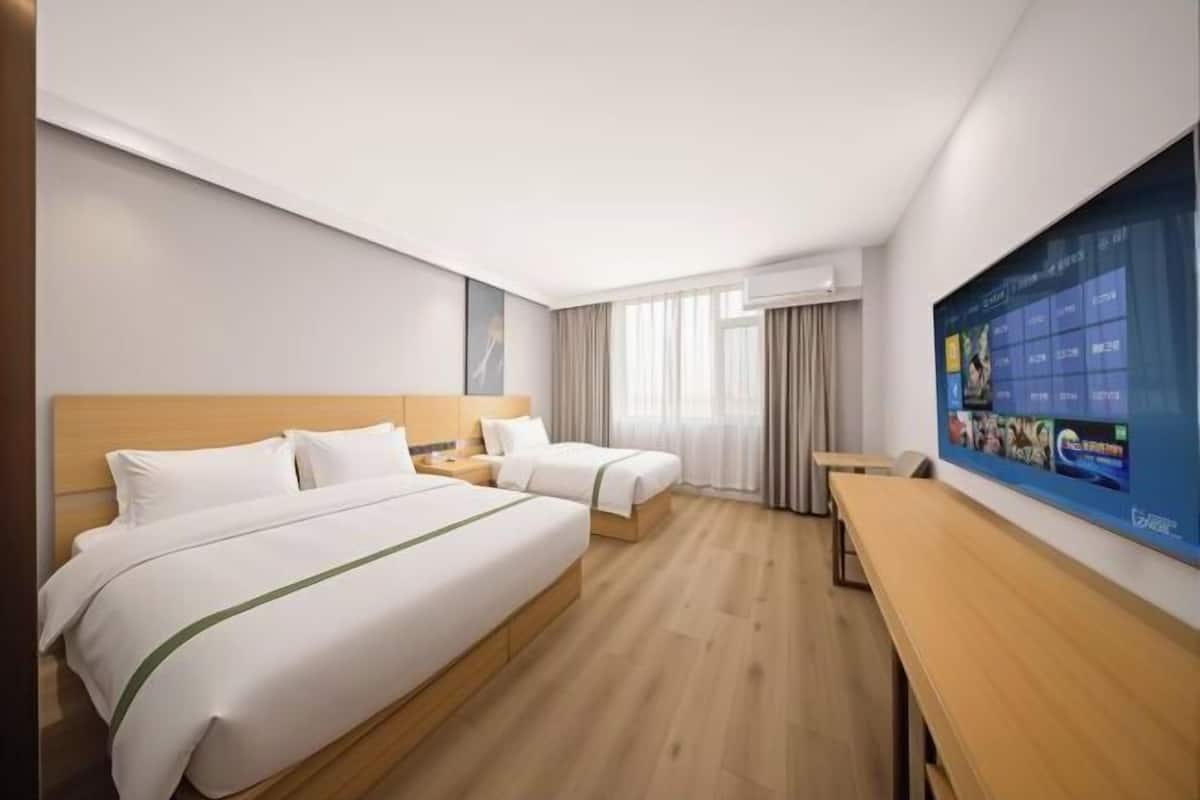 Hotellihuone, jossa on kaksi sänkyä, puinen työpöytä ja suuri näyttö, jossa näkyy elokuvien lista.