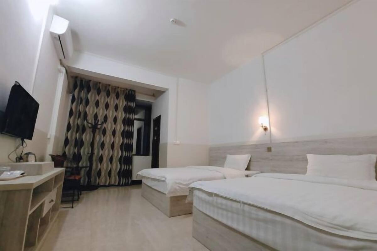 Une chambre d’hôtel avec deux lits simples, un bureau avec une chaise, un téléviseur à écran plat et un rideau à motifs.