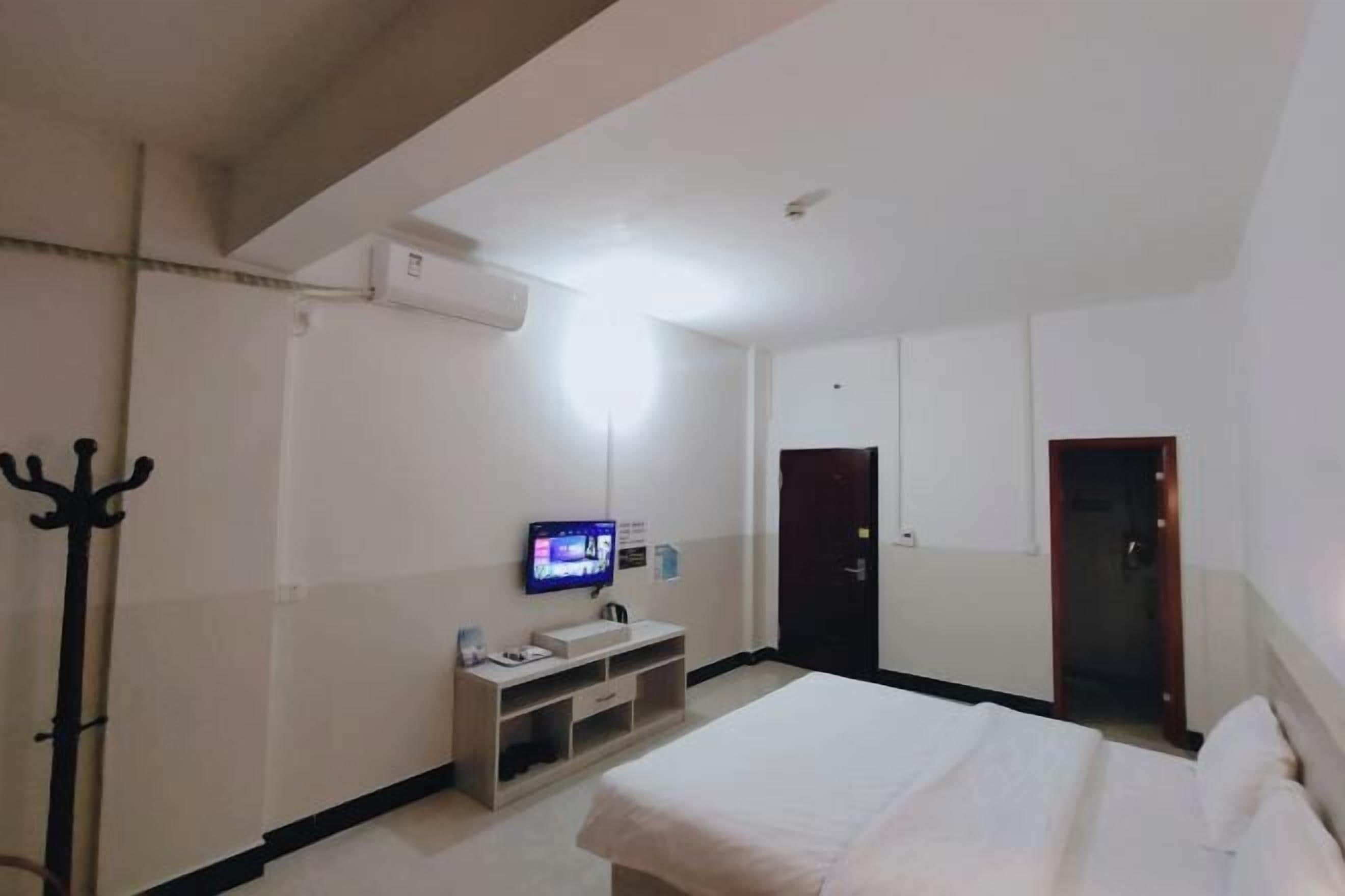 A hotel room with a bed, a TV, a coat rack, and a door.