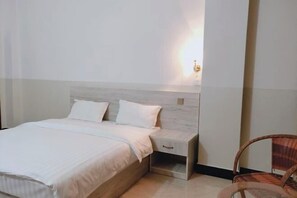 A bedroom with a bed, a nightstand, and a wicker chair. - Youke Hotel (Baise)
