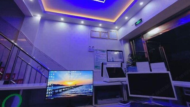 Een moderne hotel lobby met een groot scherm waarop een zonsondergang te zien is, een trap en een receptiebalie met een computer en papieren.