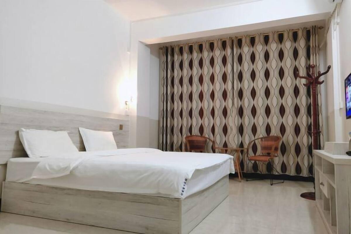 Une chambre d’hôtel avec un lit, deux chaises, une télévision et un rideau orné d’un motif géométrique.