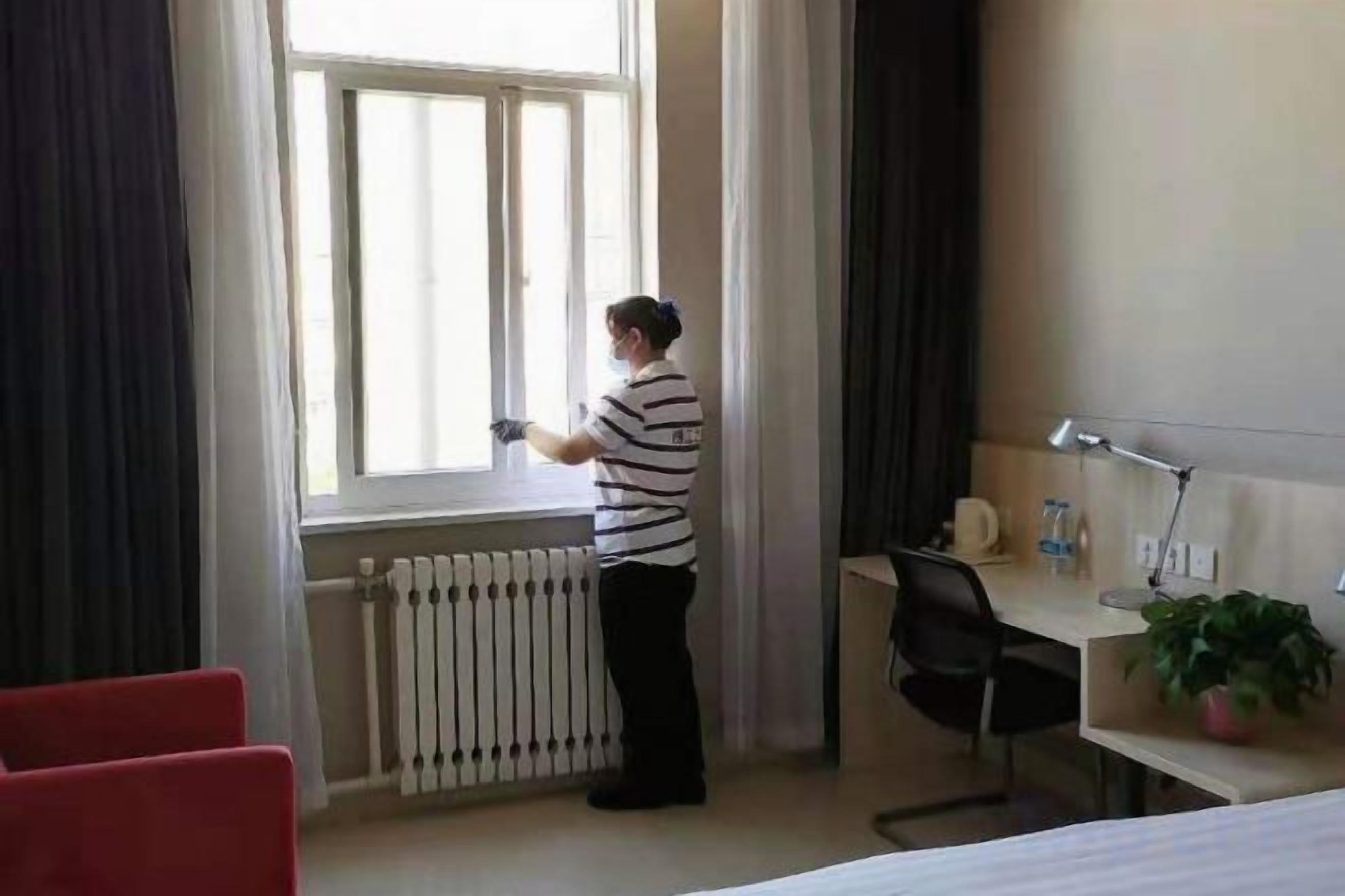 Hotellihuone, jossa on sänky, työpöytä tuolilla, ikkuna verhoilla ja patteri.