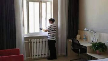 Hotellihuone, jossa on sänky, työpöytä tuolilla, ikkuna verhoilla ja patteri.