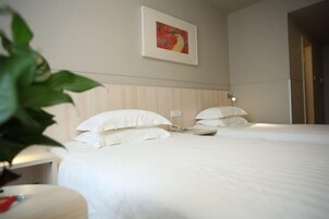 Habitación de hotel con dos camas, una mesita de noche, un cuadro en la pared y una planta en maceta.