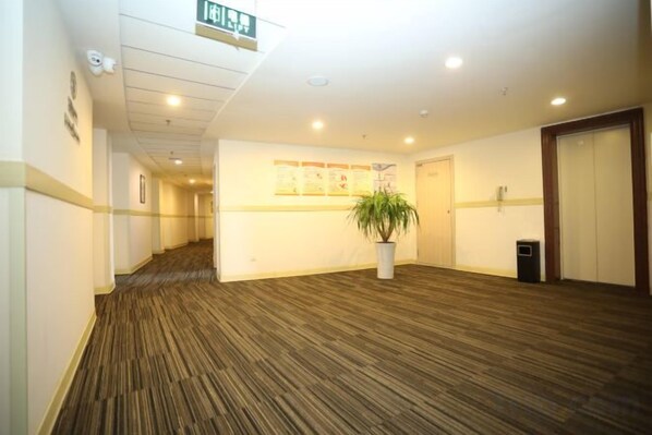 A hotel corridor with a carpeted floor, a potted plant, a trash bin, and a door.