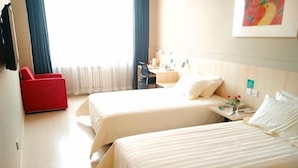 Quarto de hotel com duas camas, uma escrivaninha, uma cadeira e um poltrona vermelha.