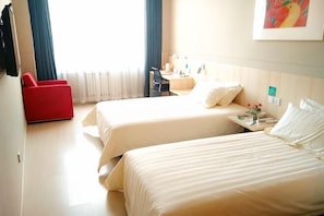 A hotel room with two beds, a desk, a chair, and a red armchair.