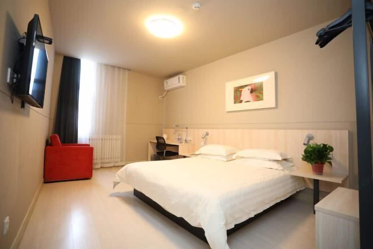 Ein Hotelzimmer mit Bett, Schreibtisch, Stuhl, Fernseher, Pflanze und einem Bild an der Wand.