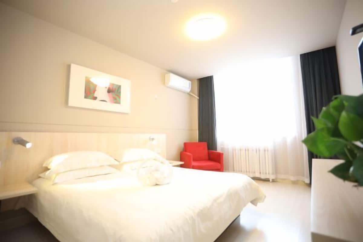 Ein Hotelzimmer mit einem Bett, einem roten Sessel, einem gerahmten Bild an der Wand und einer Klimaanlage.