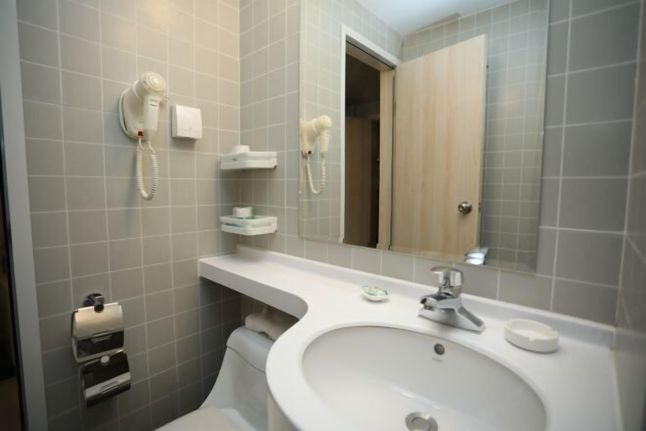 Un baño con lavamanos, espejo, toallero y secador de pelo en la pared.