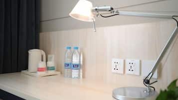 Camera d'albergo con scrivania, lampada, bollitore e due bottiglie d'acqua.