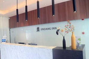 A reception desk with a logo, a vase with flowers, and a wooden panel wall. - Jin Xing Holiday Hotel (Pingliang Kongtong District Green Square Branch) (Pingliang)