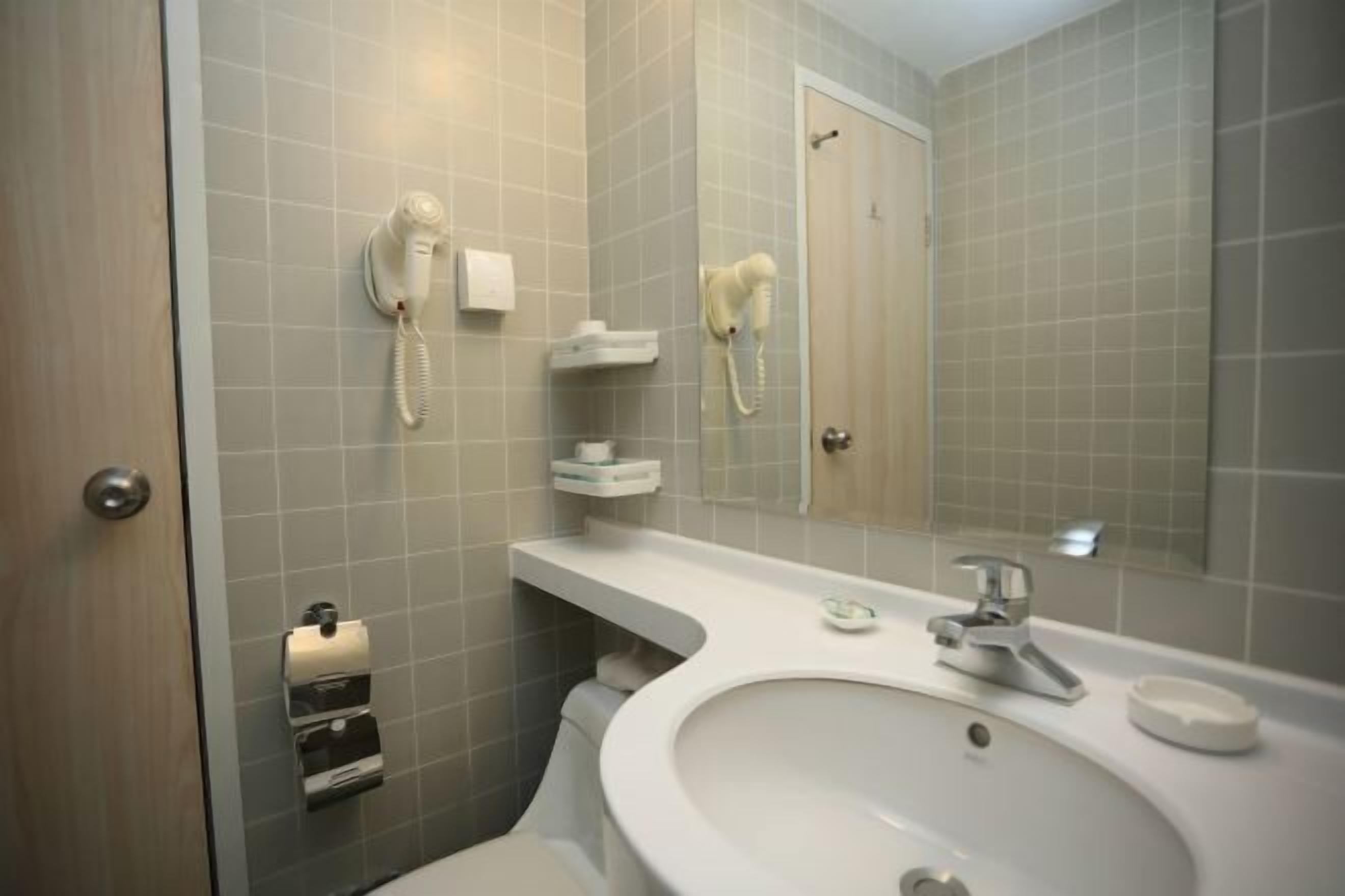 Een badkamer met een wastafel, spiegel, handdoekdispenser en een aan de muur bevestigde haardroger.