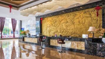 A hotel reception area with a marble counter, bar stools, and a decorative wall with relief sculptures.