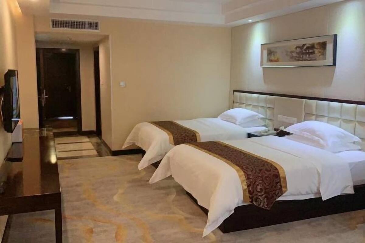 Habitación de hotel con dos camas, un televisor, piso alfombrado y un cuadro en la pared.
