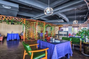 A restaurant with a modern industrial design, featuring exposed ceilings, hanging lights, and a central dining area with tables and chairs.
