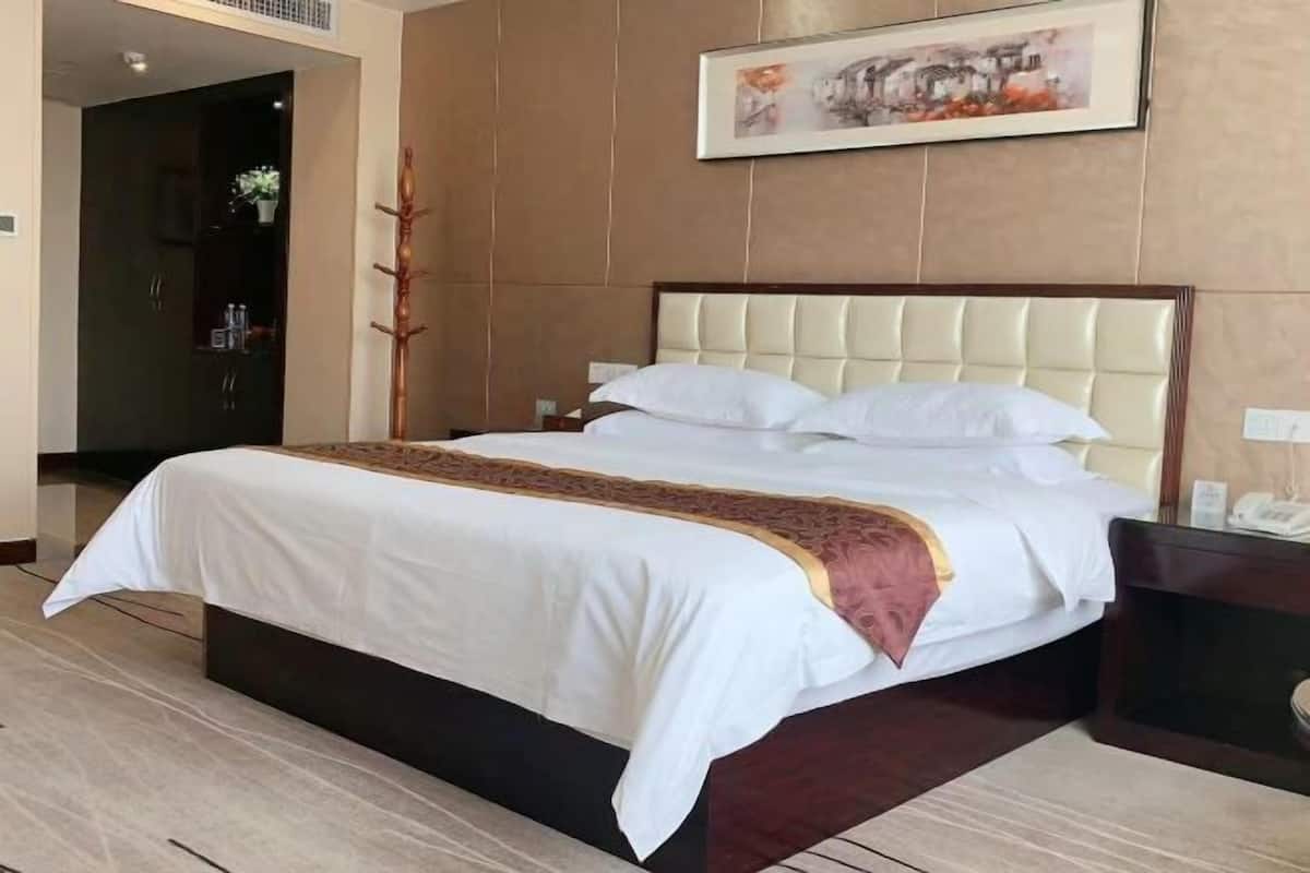 Una cama bien hecha con una colcha blanca y marrón, un cabecero de madera y una mesita de noche con un teléfono.