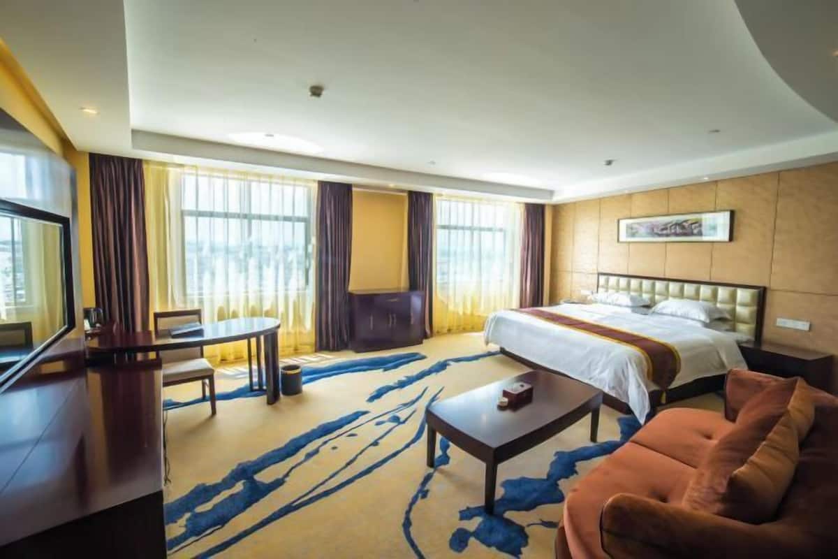 Una habitación de hotel con cama, escritorio, sofá y un amplio ventanal con cortinas.