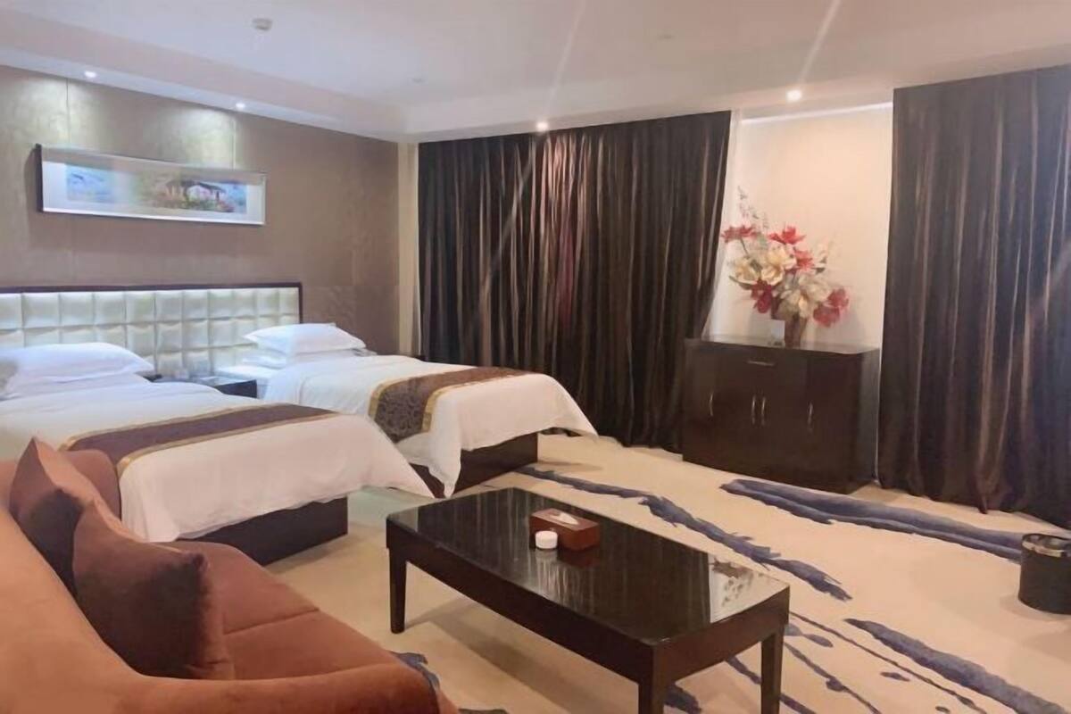 Habitación de hotel con dos camas, un sofá, una mesa de centro, un armario y un cuadro en la pared.