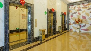 Un vestíbulo de hotel con pisos de mármol, tres ascensores y una pared decorativa con diseño de hojas.