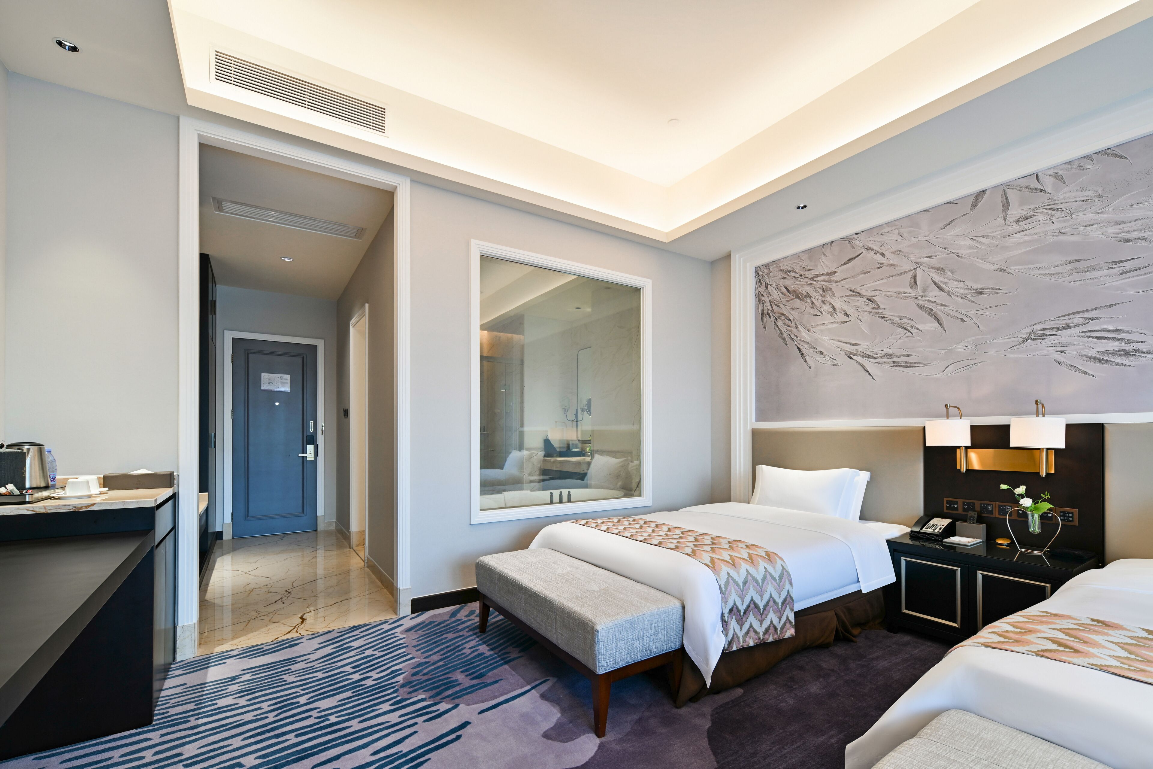 Una habitación de hotel con cama, escritorio, silla, mesita de noche y un ventanal grande.