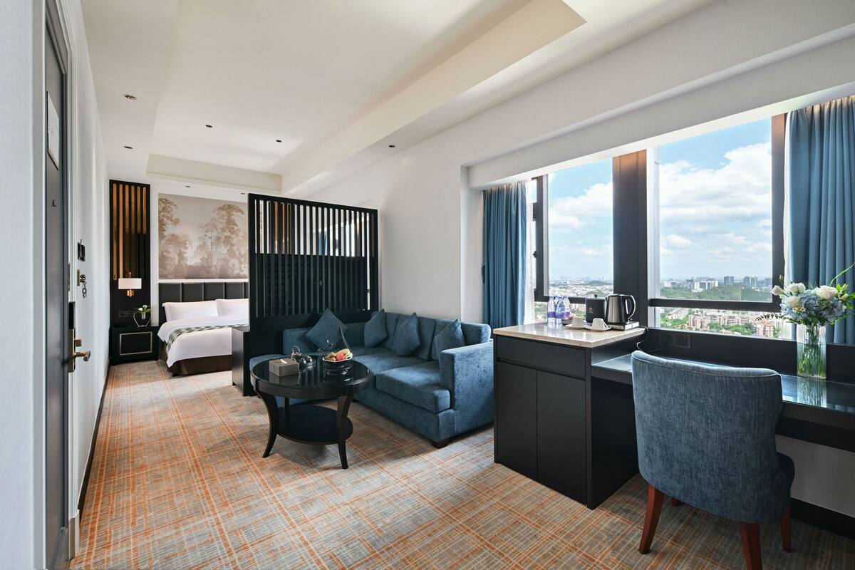 A modern hotel room with a sofa, a dining table, a chair, and a view of the city.
