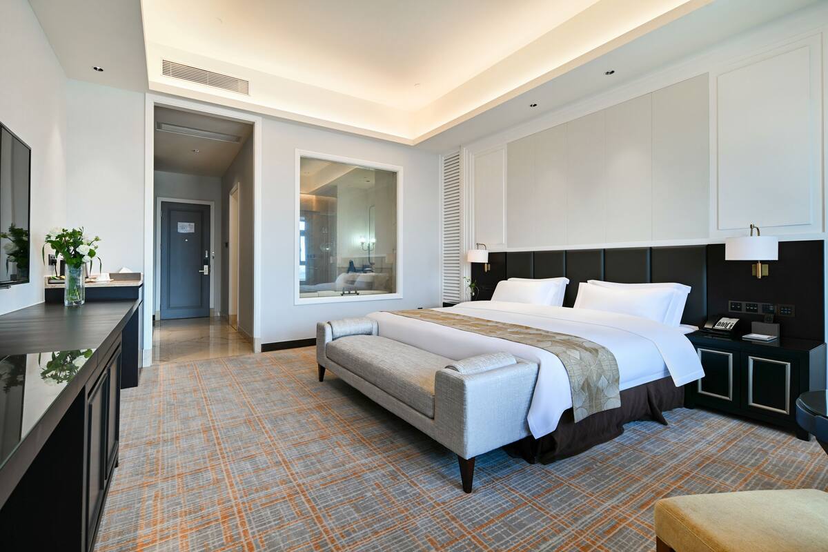 A modern hotel room with a large bed, a bedside table, a desk, and a view of the bathroom.
