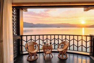 Un balcón con sillas de mimbre y una pequeña mesa, con vistas a una masa de agua tranquila y montañas distantes al atardecer.