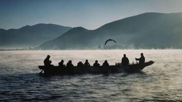 A boat with several people on a calm body of water, surrounded by misty mountains.