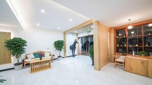 A spacious lobby with a wooden reception desk, a seating area with a bench and chairs, and potted plants.