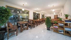 A spacious indoor area with wooden tables and chairs, potted plants, and a bookcase.