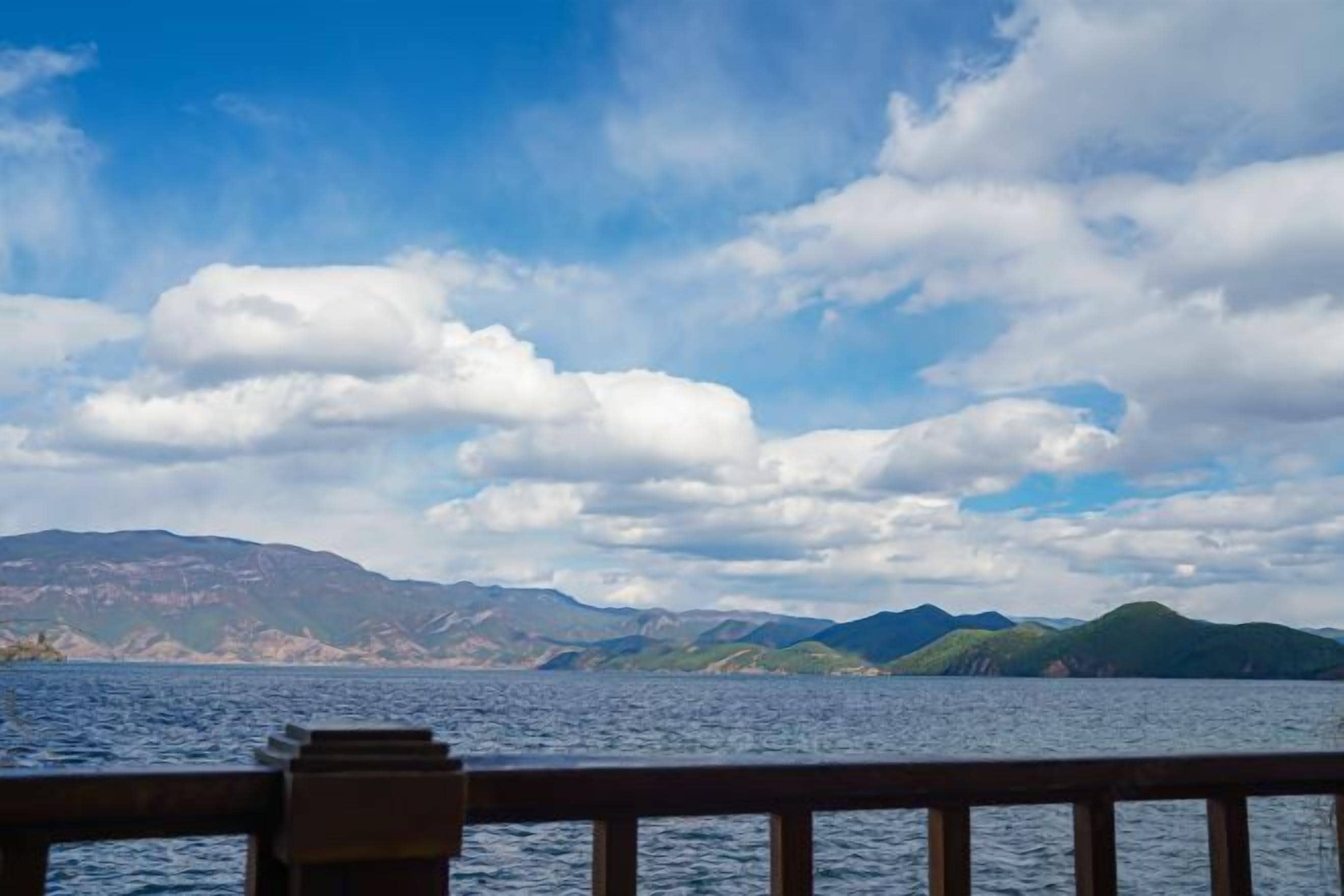 A view of a body of water with mountains in the background and a wooden railing in the foreground.