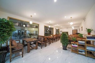 A spacious indoor area with multiple wooden tables and chairs, a marble floor, and a variety of potted plants.