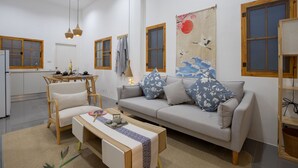 Un salon moderne avec un canapé, un fauteuil et une table basse, un coin repas avec une table et des chaises, et une cuisine en arrière-plan.