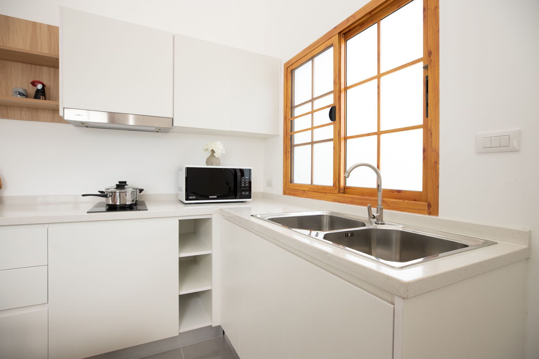 A compact kitchen with white cabinetry, a microwave, a sink, and a window with wooden frames.