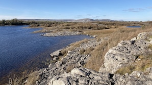 Un paisaje natural con un río, terreno rocoso y colinas a lo lejos.