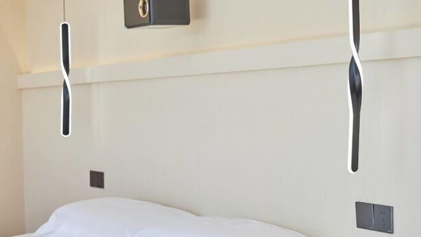 A hotel room with a bed, a wall-mounted light fixture, and a power outlet. - Otter Home (Zhoushan)