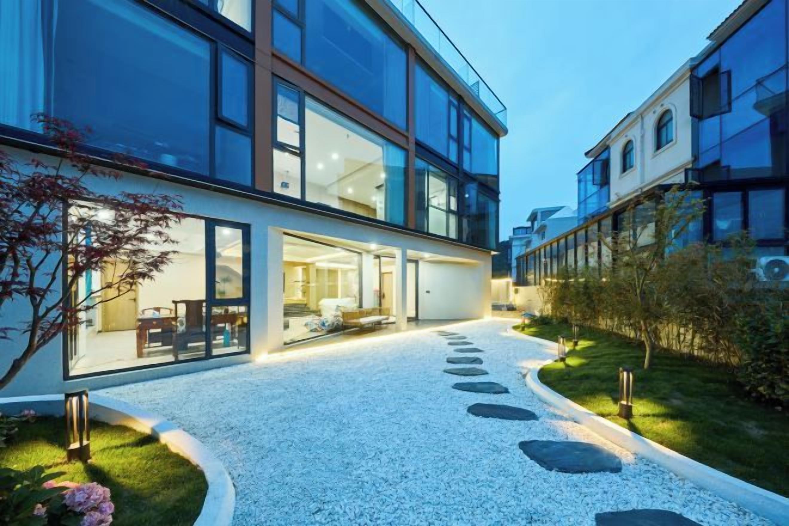 Un edificio moderno con ventanas amplias, un sendero de grava y un jardín bien cuidado.