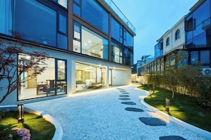 A modern building with large windows, a gravel pathway, and a well-maintained garden. - Otter Home (Zhoushan)