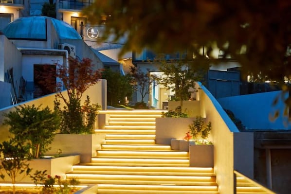 Una escalera conduce a un edificio con una estructura de cúpula, rodeado de vegetación y con escalones iluminados.