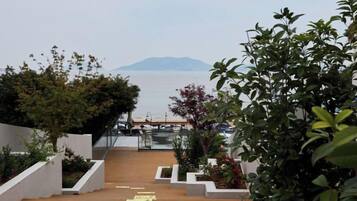 A wooden staircase leading to a terrace with a view of the sea and a distant mountain.