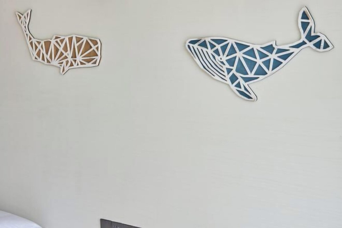 Two whale-shaped wall decorations, one in a light color and the other in blue, on a plain wall.